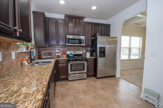 kitchen with stainless steel appliances, dark brown cabinets, sink, and light stone counters