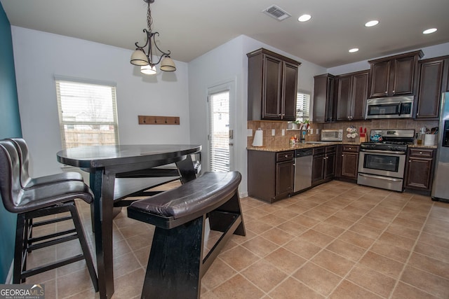 kitchen with pendant lighting, stainless steel appliances, light stone counters, tasteful backsplash, and dark brown cabinetry