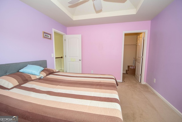 bedroom featuring a spacious closet, light colored carpet, ceiling fan, a raised ceiling, and a closet