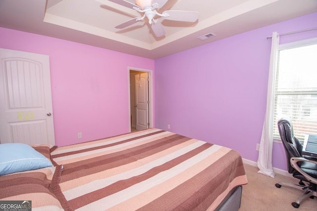 carpeted bedroom with multiple windows, ceiling fan, and a tray ceiling