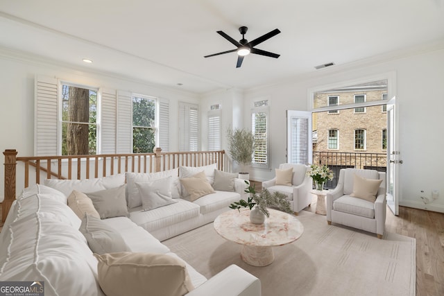 living room featuring light wood-style flooring, visible vents, baseboards, and ornamental molding