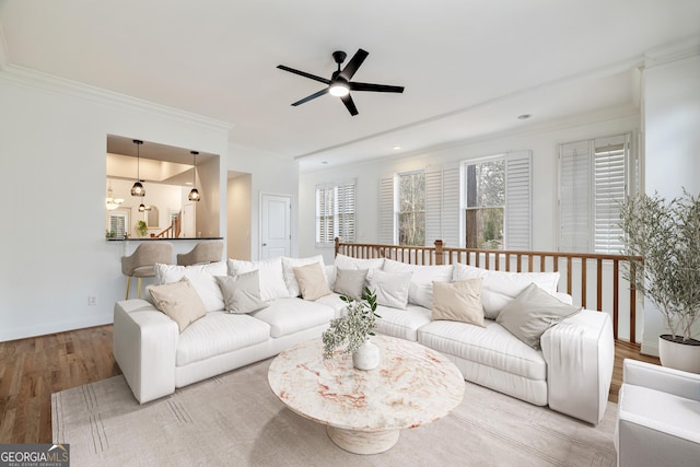 living area with baseboards, wood finished floors, a ceiling fan, and crown molding