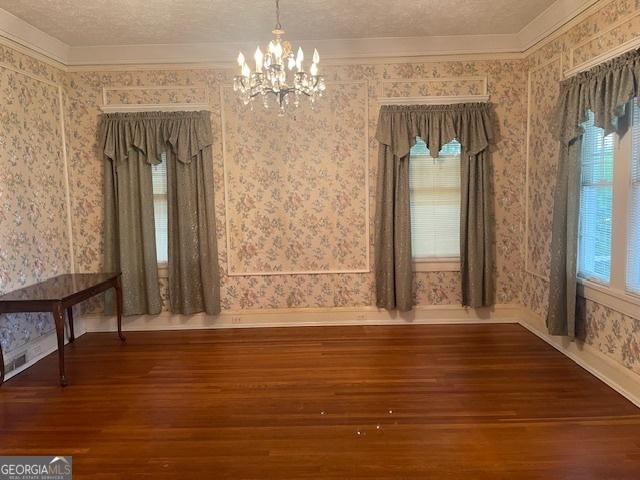 unfurnished dining area featuring dark wood-style flooring, ornamental molding, a textured ceiling, a chandelier, and wallpapered walls