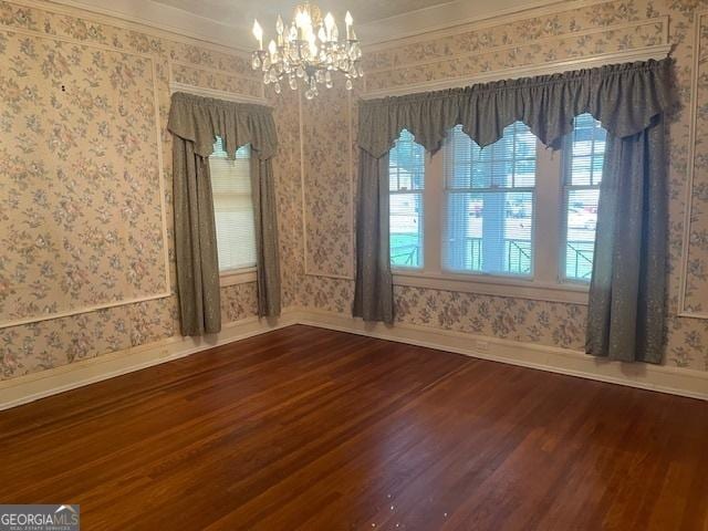 spare room with a chandelier, wood finished floors, crown molding, and wallpapered walls