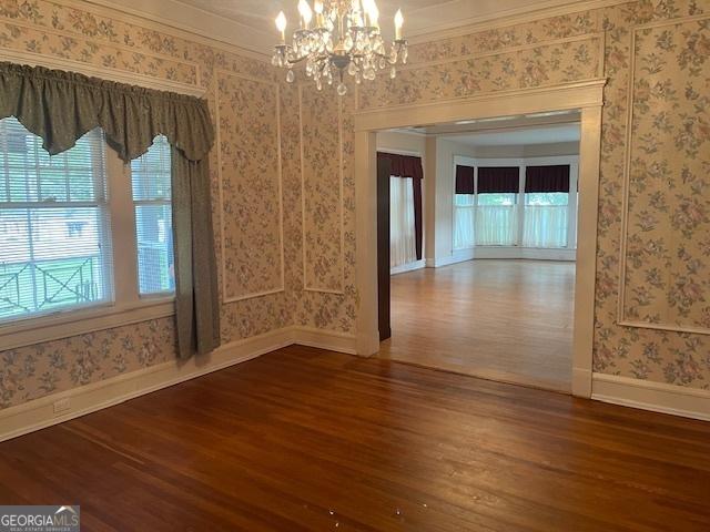 unfurnished dining area with wallpapered walls, baseboards, wood finished floors, an inviting chandelier, and crown molding