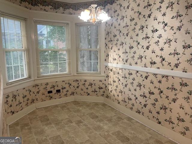 unfurnished dining area featuring baseboards, wainscoting, an inviting chandelier, and wallpapered walls