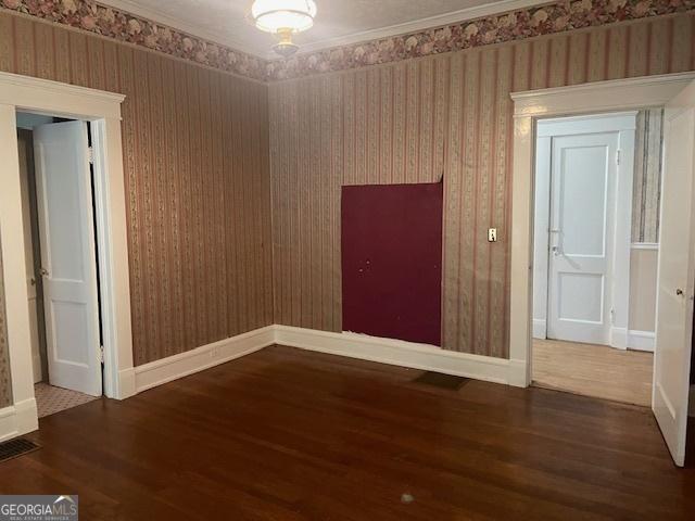 empty room featuring baseboards, ornamental molding, dark wood-style flooring, and wallpapered walls