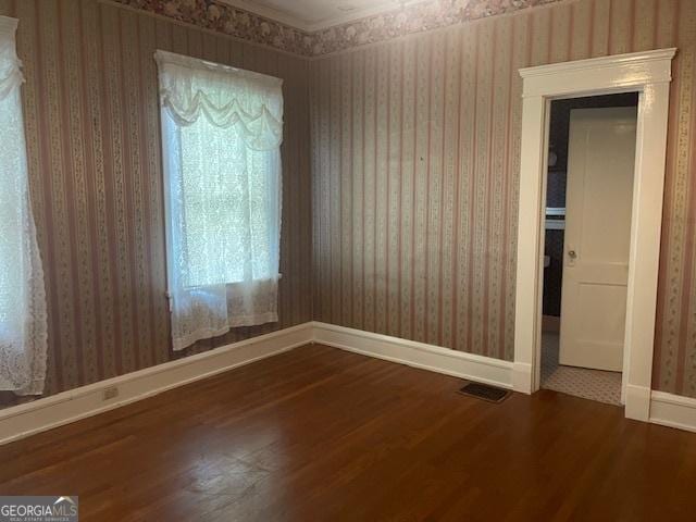 unfurnished room featuring wood finished floors, visible vents, baseboards, and wallpapered walls