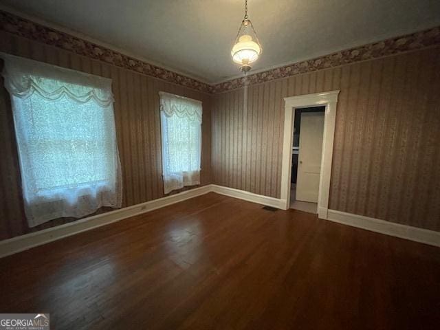 empty room featuring wood finished floors, baseboards, and wallpapered walls