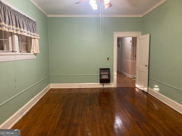 empty room with baseboards, crown molding, heating unit, and wood finished floors