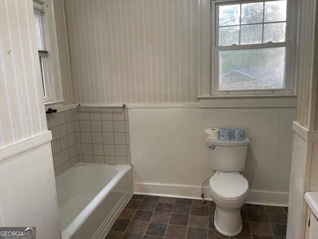 bathroom with baseboards, tile patterned floors, toilet, and a tub