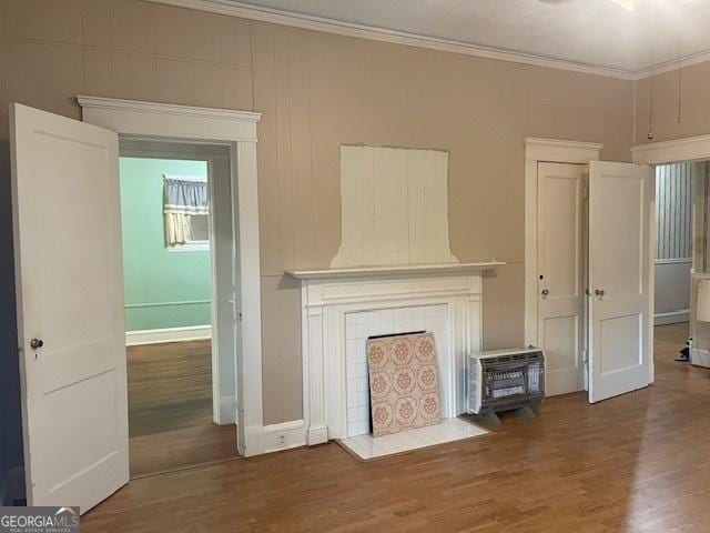 unfurnished living room with a tile fireplace, crown molding, baseboards, and wood finished floors