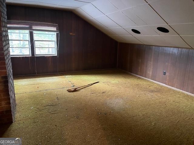 bonus room with vaulted ceiling and wood walls