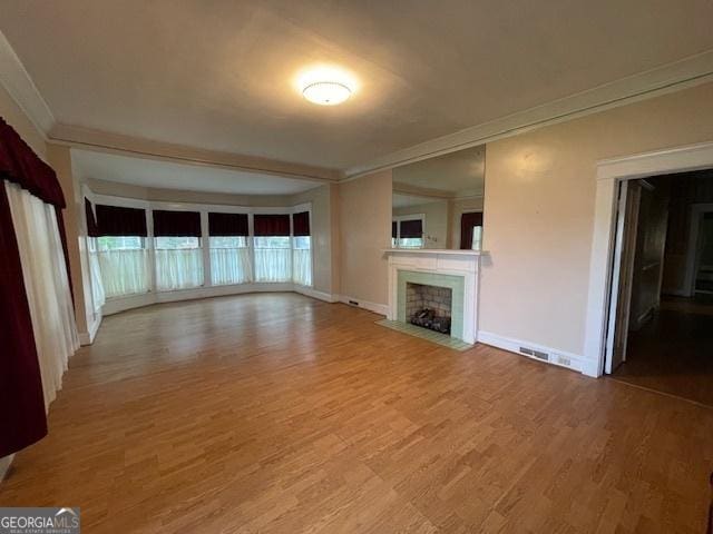 unfurnished living room with ornamental molding, wood finished floors, a fireplace with flush hearth, and baseboards