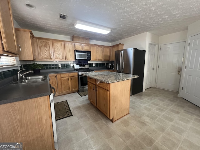 kitchen featuring a kitchen island, appliances with stainless steel finishes, sink, decorative backsplash, and a textured ceiling