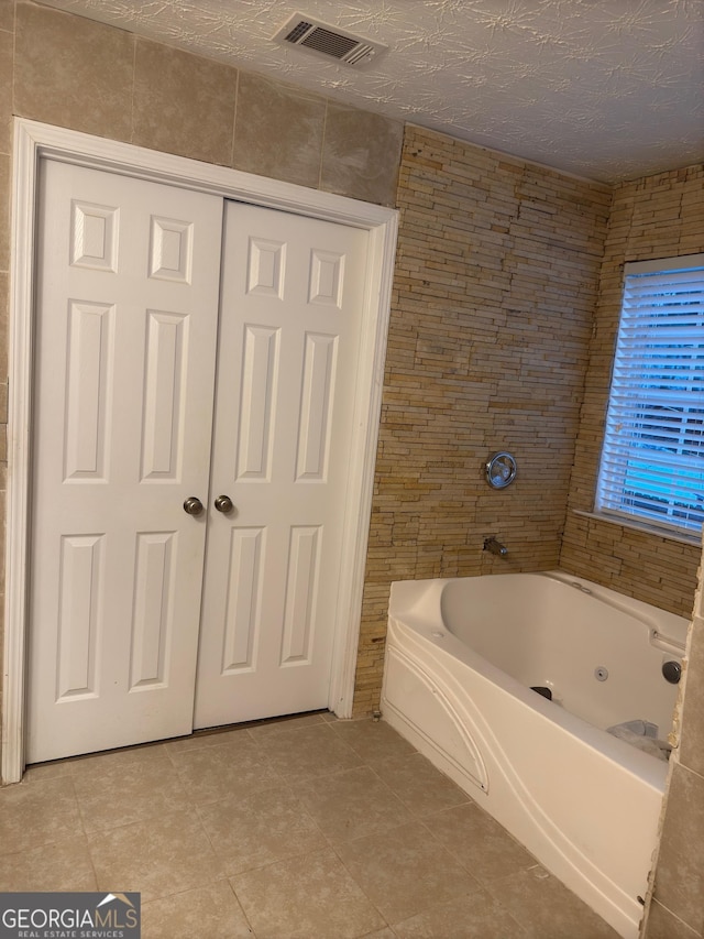 bathroom with tile patterned flooring, tile walls, a textured ceiling, and a bathtub