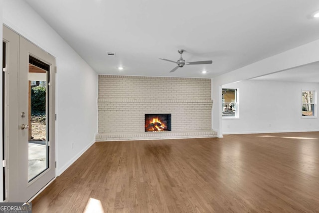 unfurnished living room featuring brick wall, dark hardwood / wood-style floors, ceiling fan, and a brick fireplace