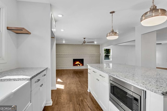 kitchen featuring stainless steel microwave, white cabinets, light stone counters, and decorative light fixtures