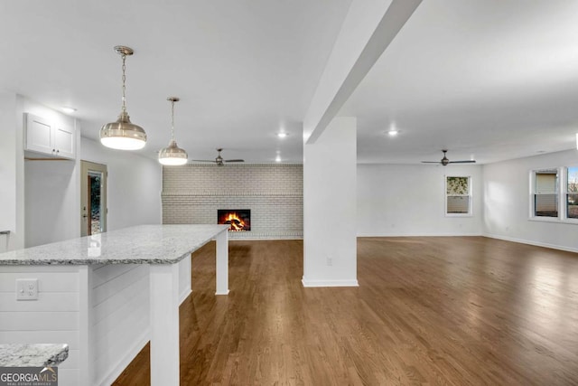 kitchen featuring dark wood-type flooring, a brick fireplace, hanging light fixtures, a kitchen breakfast bar, and white cabinets