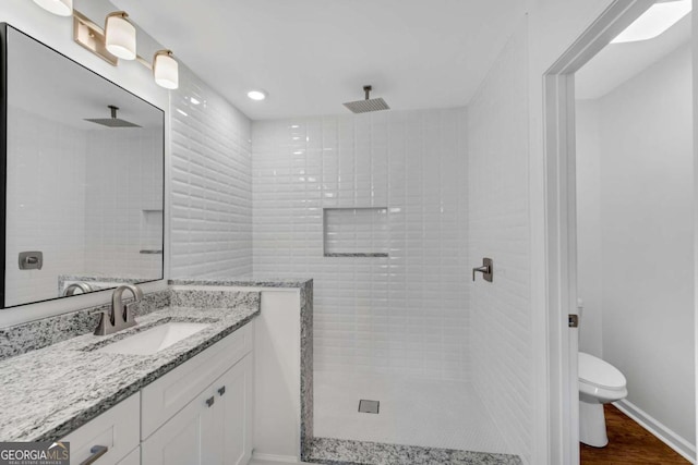 bathroom featuring a tile shower, hardwood / wood-style floors, vanity, and toilet