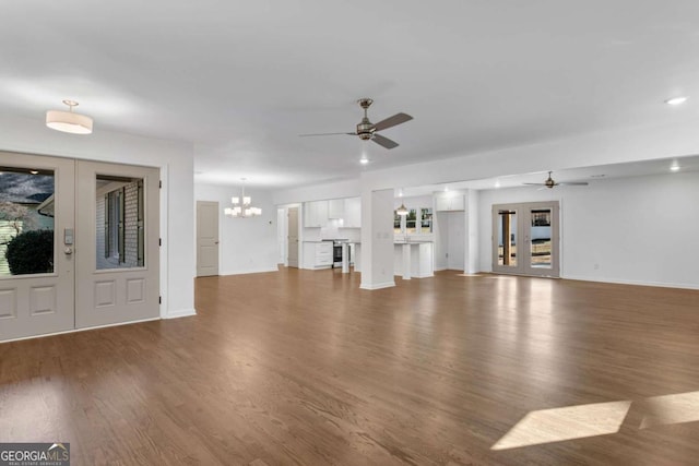 unfurnished living room with dark wood-type flooring, ceiling fan with notable chandelier, and french doors