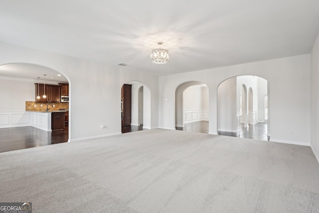 unfurnished living room featuring a chandelier, visible vents, dark carpet, and baseboards