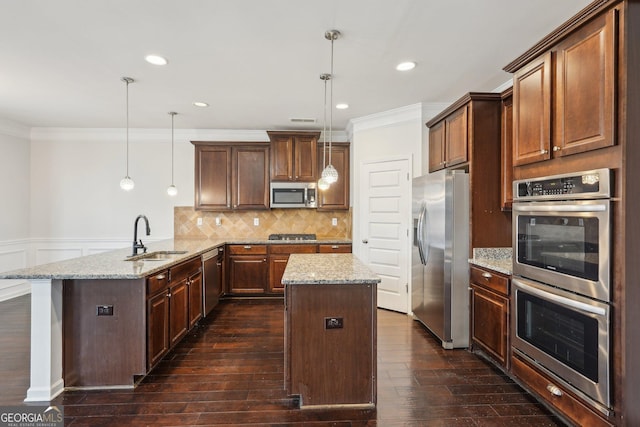 kitchen featuring a peninsula, stainless steel appliances, a sink, light stone countertops, and decorative light fixtures