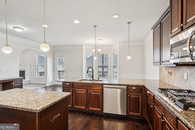 kitchen with stainless steel appliances, a sink, open floor plan, an island with sink, and decorative light fixtures