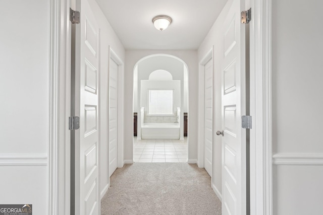 hallway featuring arched walkways, light tile patterned flooring, and light colored carpet