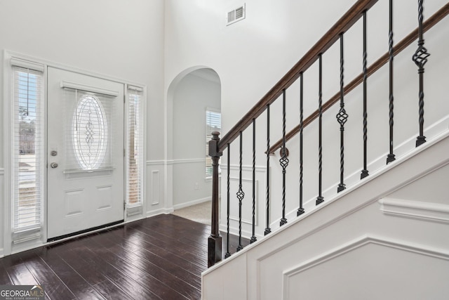 foyer with stairs, visible vents, arched walkways, and wood finished floors