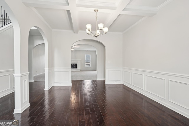 unfurnished dining area featuring dark wood finished floors, coffered ceiling, a glass covered fireplace, beamed ceiling, and an inviting chandelier