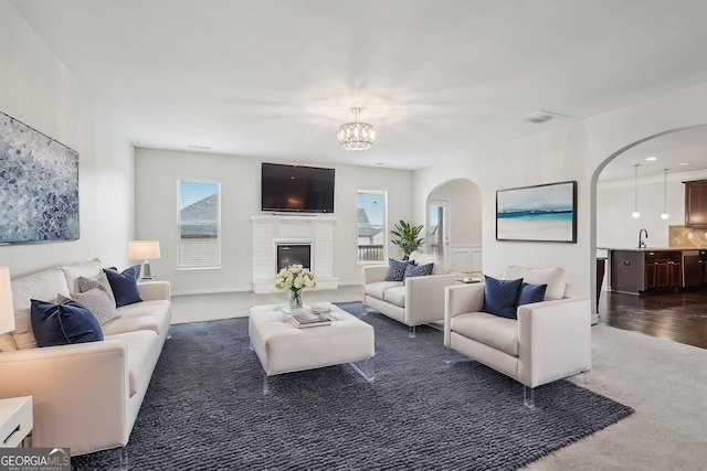 living room featuring a brick fireplace, a healthy amount of sunlight, dark carpet, and visible vents