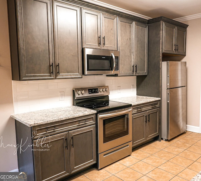 kitchen with appliances with stainless steel finishes, backsplash, light tile patterned floors, dark brown cabinetry, and light stone counters