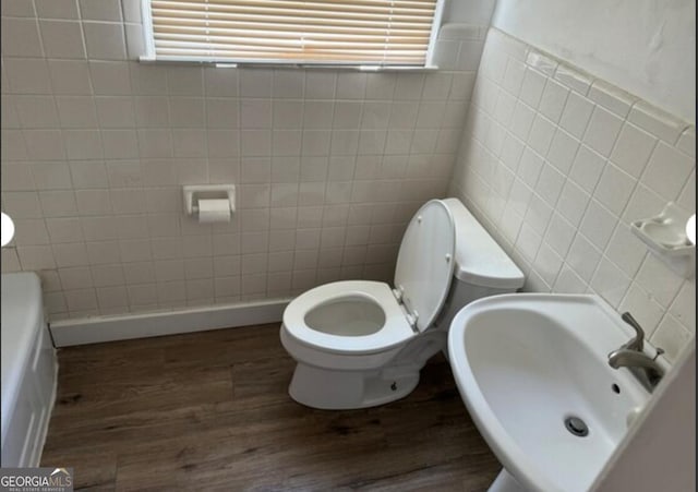 bathroom featuring wood-type flooring, toilet, tile walls, and a washtub