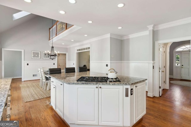 kitchen with white cabinetry, a kitchen island, stone counters, hardwood / wood-style flooring, and stainless steel gas stovetop