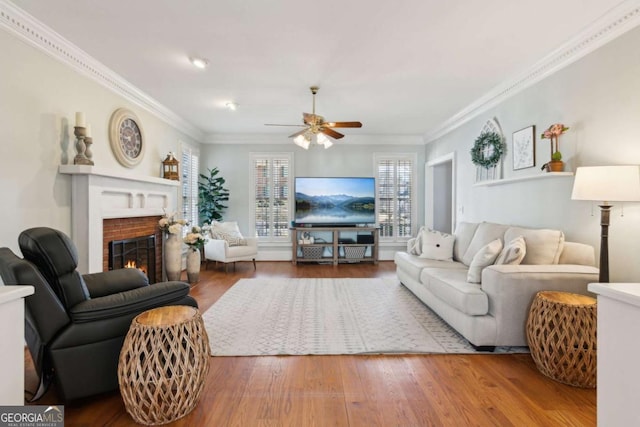 living room with crown molding, ceiling fan, wood-type flooring, and a fireplace