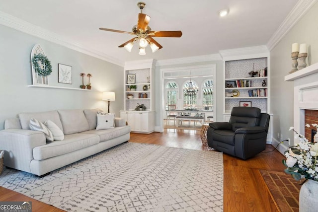 living room with hardwood / wood-style flooring, ornamental molding, ceiling fan with notable chandelier, and built in shelves