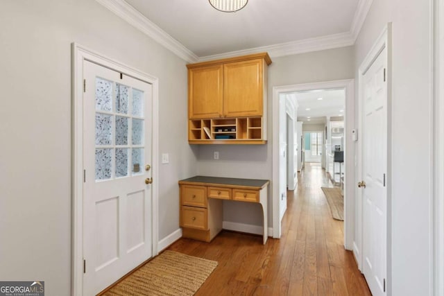 interior space featuring built in desk, ornamental molding, and light wood-type flooring