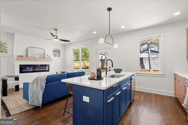 kitchen with blue cabinets, a sink, a breakfast bar area, light countertops, and dark wood-style flooring