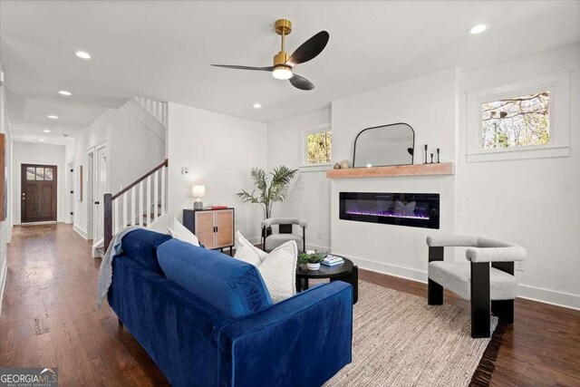 living room featuring a glass covered fireplace, a healthy amount of sunlight, stairway, and wood finished floors