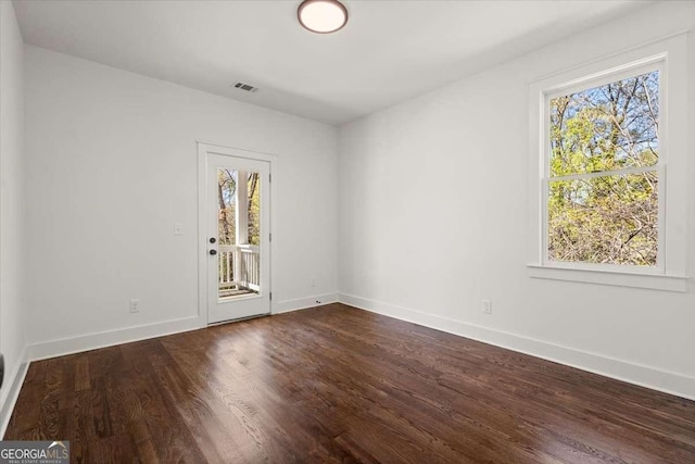 spare room featuring dark wood-type flooring, baseboards, visible vents, and a wealth of natural light