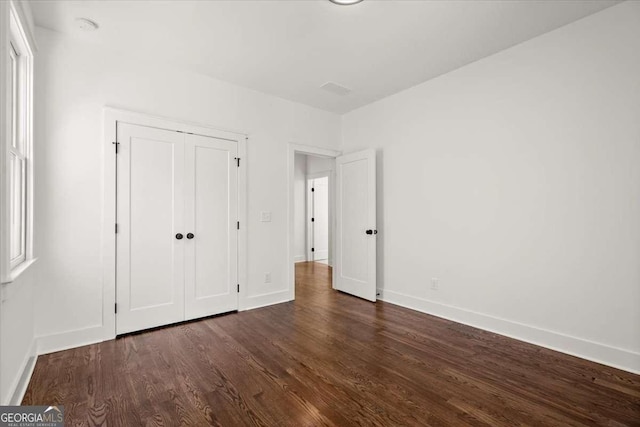 unfurnished bedroom featuring dark wood-style floors, baseboards, and a closet