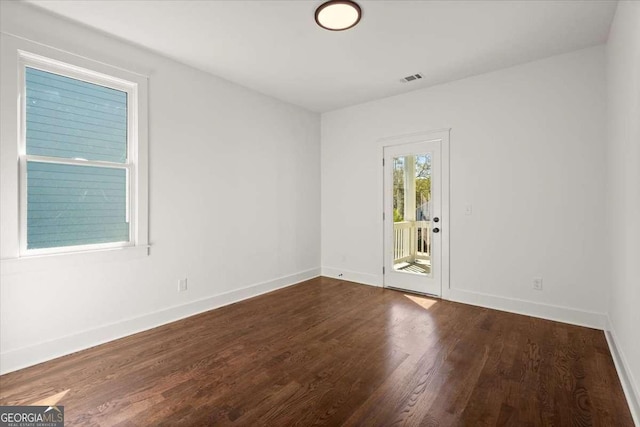 spare room with dark wood-style floors, visible vents, and baseboards