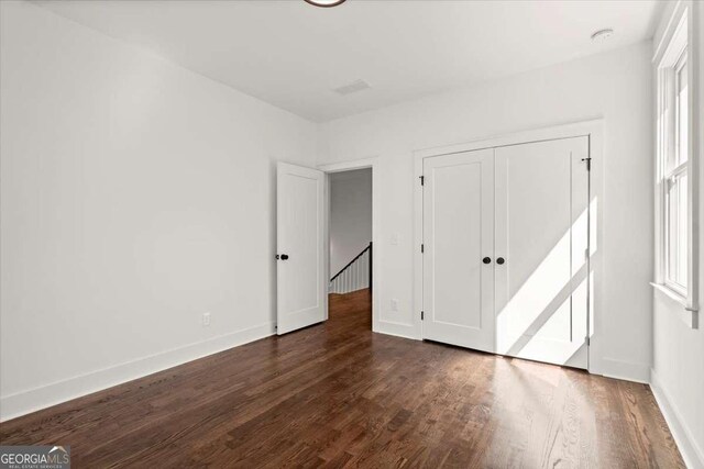 unfurnished bedroom with a closet, multiple windows, dark wood-type flooring, and baseboards