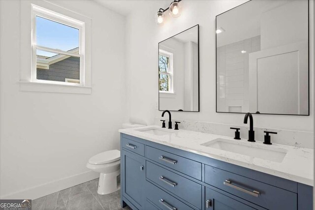 bathroom with a sink, baseboards, toilet, and double vanity