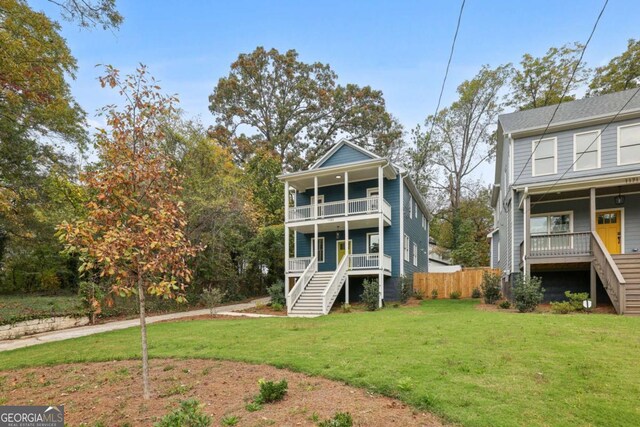 rear view of property featuring stairway, a balcony, fence, a porch, and a yard