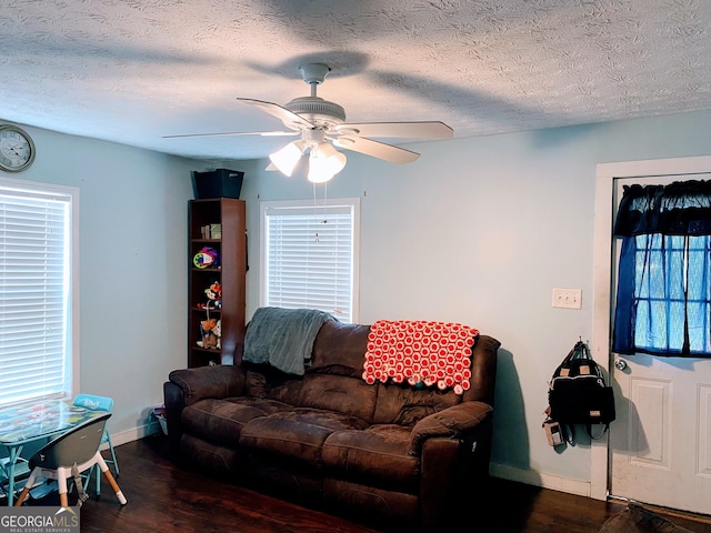 living room with a textured ceiling, dark wood-type flooring, and ceiling fan