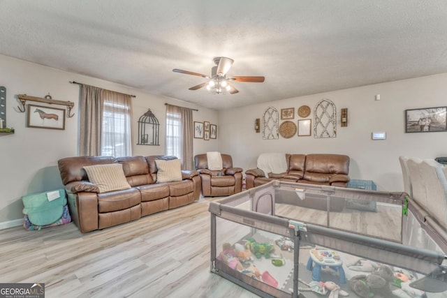 living room featuring ceiling fan, a textured ceiling, and light wood-type flooring