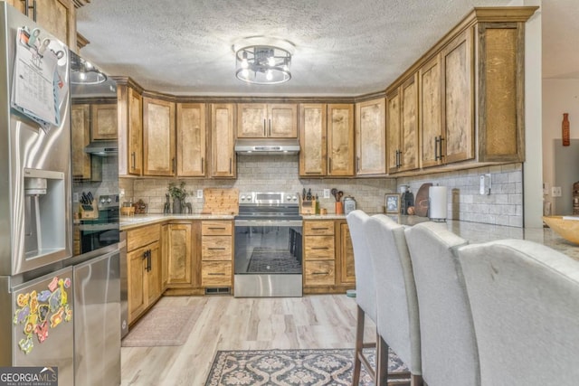 kitchen featuring decorative backsplash, appliances with stainless steel finishes, light hardwood / wood-style flooring, and a textured ceiling