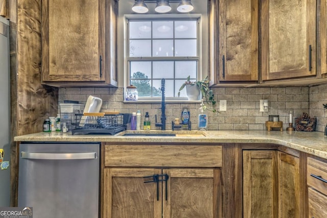 kitchen with light stone counters, sink, backsplash, and stainless steel dishwasher